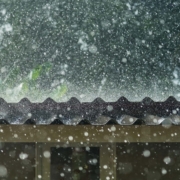 Front view of hail and rain coming down on metal roof during a storm