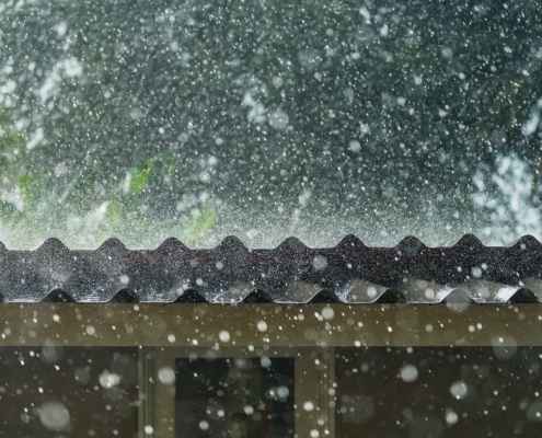 Front view of hail and rain coming down on metal roof during a storm