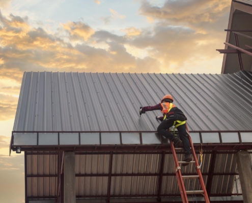 Construciton worker installing metal roof on commercial building