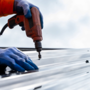 Roofer worker using air or pneumatic nail gun and installing metal sheet on top of the new roof