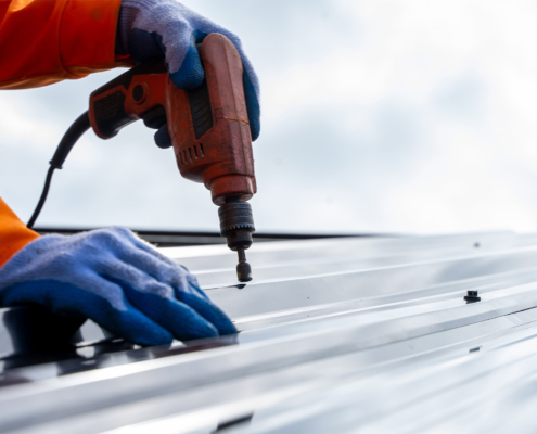 Roofer worker using air or pneumatic nail gun and installing metal sheet on top of the new roof